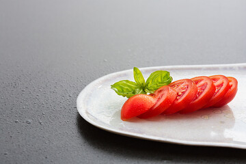 Fresh and tasty tomato with basil on white dish on black tabletop. Healthy vegan Food.