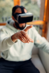 Selective focus at hand making gesture in air, virtual reality. Young man wearing VR goggles while playing