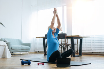 elderly woman sitting in a yoga pose in front of an open laptop.