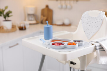 High chair with food in baby tableware on white tray indoors