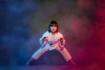 Fototapeta na wymiar 5-year-old elementary school girl, in kimono, practicing martial arts among smoke and colored lights.