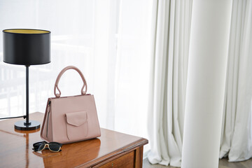 A handbag is placed on a table , Pink side bag placed on a table, table for living room slightly, side bag on wooden table, black table lamp, hotel room, boutique hotel
