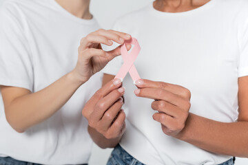 Obraz na płótnie Canvas Cropped view of women holding ribbon of breast cancer awareness isolated on grey.