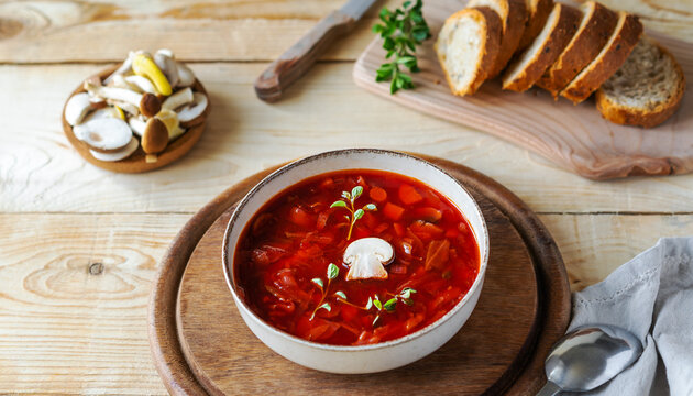 Vegan beetroot soup with mushrooms in a bowl and bread on a wooden background