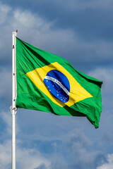 The Brazilian flag fluttering on the pole. Blue sky.