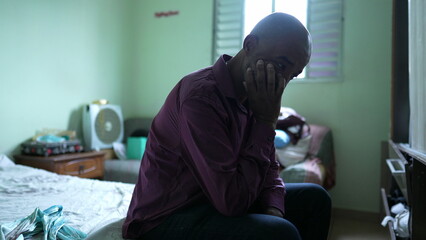A worried black senior man sitting by bedside suffering from depression