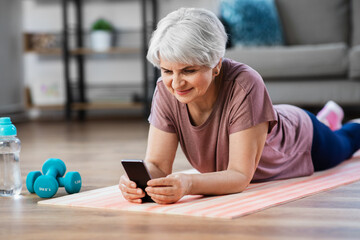 sport, fitness and healthy lifestyle concept - smiling senior woman with smartphone exercising on mat at home