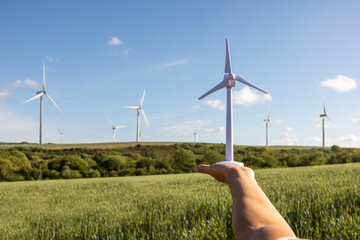Engineer in the fields holding a wind turbine model with real ones on background