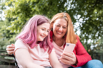 Woman and girl looking at mobile phone at park and smiling