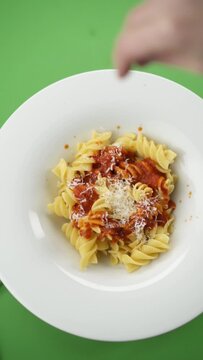 Vertical video: parmesan cheese falls on pasta in a plate