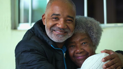 A black adult son hugging senior mother posing for camera together
