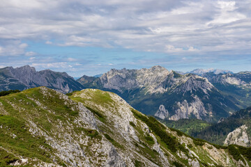 Fototapeta na wymiar Panoramic view from Messnerin on the alpine mountain chains in Styria, Austria, Hochschwab region. Hills overgrown with small bushes, higher parts rocky and bare. Summer day. Hiking in Alps, Tragoess