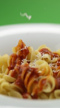 Vertical video: parmesan cheese falls on pasta in a plate