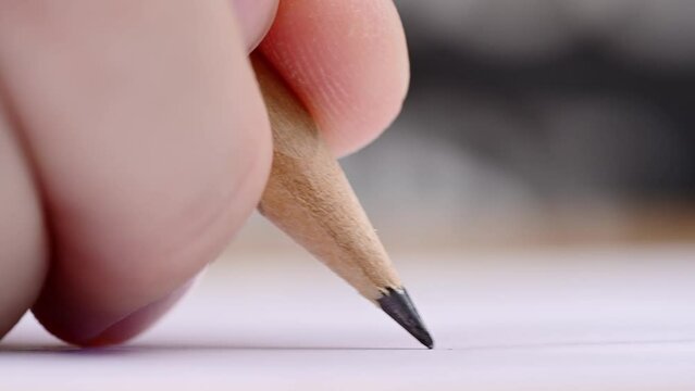Macro of pencil writing or drawing. Unknown person drawing line or letter on white paper.