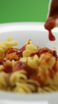 Vertical video: tomato paste falls on pasta in a plate