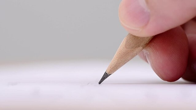 Macro of pencil writing or drawing. Unknown person drawing line or letter on white paper.