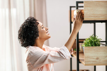home improvement and people concept - happy smiling woman arranging books on shelving