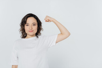 Young woman in white t-shirt showing muscles isolated on grey.