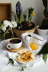 Cozy spring morning at home. Coffee, pancakes with honey. Hyacinth flowers, daffodils in a wicker basket and a wooden tray on background. Warm mood.