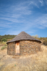 Old cabin or hut with a round shape and slate stone walls and a broom and straw roof