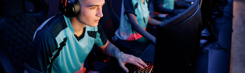 Naklejka premium Young esports player concentrated on game wearing wired headset while playing online multiplayer game in cyber club