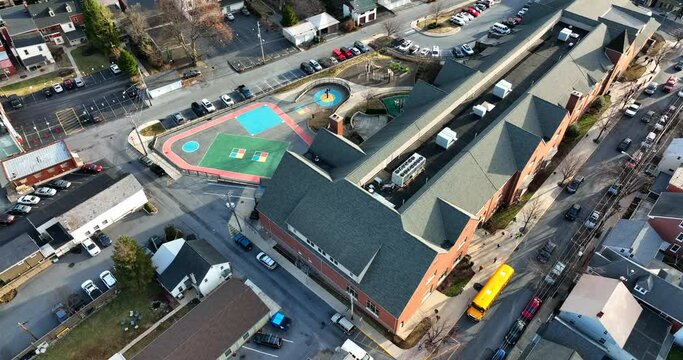 Public elementary school and painted playground for recess. Urban town school bus drop off of students in winter morning. Aerial view.