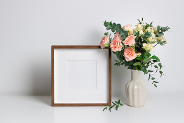 Square wooden frame mockup for artwork, photo, print and painting presentation. White interior walll with roses flowers bouquet.