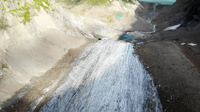 Aerial view with pan up from the crevasses of Stein glacier up towards heart shaped lake at Sustenpass, Switzerland with a view of tall peaks of the Swiss Alps