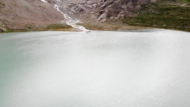 Aerial flyover above the heart shaped lake towards Stein glacier at Sustenpass, Switzerland with a view of surrounding tall peaks of the Swiss Alps