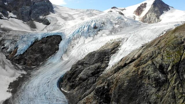 Aerial view with pan down from Stein glacier over the crevasses towards the heart shaped lake at Sustenpass, Switzerland with a view of tall peaks of the Swiss Alps