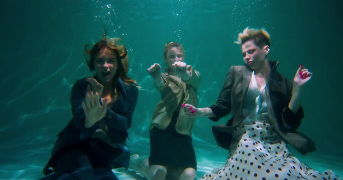 Three young fun beautiful happy business women in formal clothes dance together underwater celebrating win slow motion.