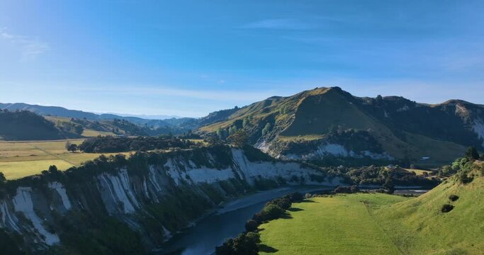 Flying around white cliffs over Rangitikei river lush fields - New Zealand