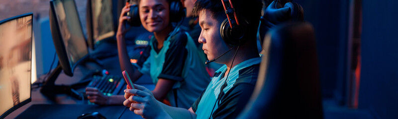 Side view of Asian cybersport gamer in headphones playing mobile game on cellphone in contemporary e-sports club © Yaroslav Astakhov