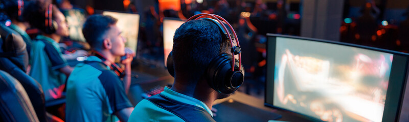Rear view of professional cybersport gamer playing video games and wearing headphones in dark...
