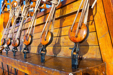 Pulleys on an old ship. Traditional wooden sailboat. Part of an old wooden ship with ropes tied in knots and wooden fasteners. Rigging on an old wooden ship.