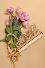 a bouquet of pink tulips on a beige background and a wooden craft inscription love