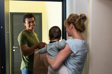 Delivery man delivers package to a mother with a baby in her arms.