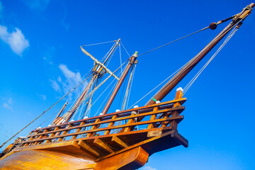 An old wooden caravel ship with folded sails against a blue sky with white clouds.