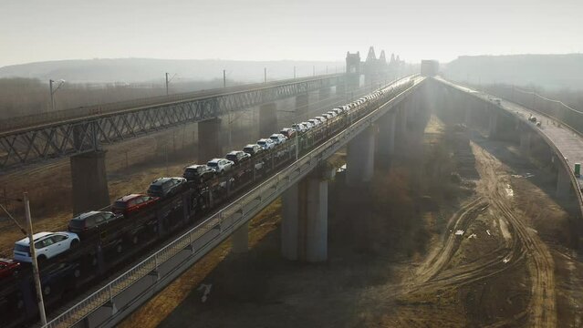4k aerial video with a cargo train full with Dacia cars going from the factory to Constanta seaport via Cernavoda Bridge in Romania. 2022.
