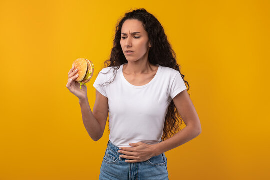 Sad Young Lady Holding Burger Suffering From Stomachache