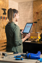 Woman carpenter in workshop holding and looking at tablet