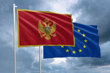 Montenegro and EU flag together next to each other on a flagpole. Montenegro flag in front of a European Union flag on a stormy sky background