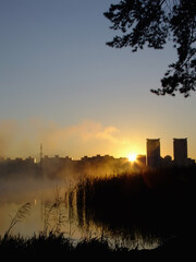 Sunrise on a foggy lake. The morning city in a haze in the background. Mirror surface of water