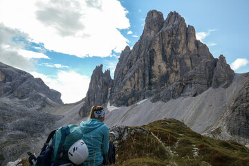 Fototapeta premium A woman in blue pullover resting under the foot of high Italian Dolomites. There are many sharp peaks in front of her. She is recharging before the further climb. Lots of lose stones and landslides.