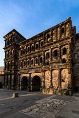 Fototapeta na wymiar The “Porta Nigra“ (Latin black gate) is a large Roman city gate in Trier, Germany. Largest Roman city gate north of the Alps. Historic landmark monument sight in town centre with warm evening light.