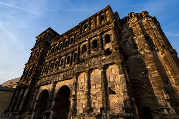 The “Porta Nigra“ (Latin black gate) is a large Roman city gate in Trier, Germany. Largest Roman city gate north of the Alps. Historic landmark monument sight in town centre with warm evening light.