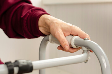 Hands of a senior woman on the handles of a walker. Rehabilitation and healthcare concept.