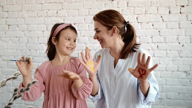 Young mother and brunette daughter smiling and painting palms with paint.
