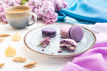 Obraz na płótnie Canvas Purple macarons or macaroons cakes with cup of coffee on a white concrete background. Side view.