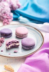 Obraz na płótnie Canvas Purple macarons or macaroons cakes with cup of coffee on a white concrete background. Side view, selective focus.